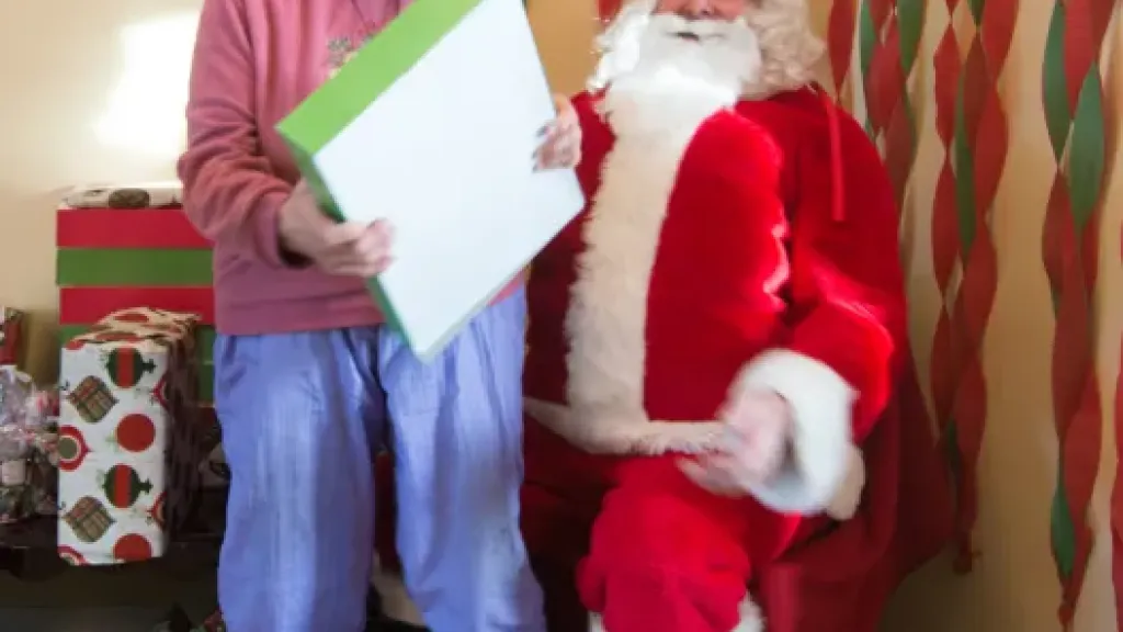Person smiling while holding present and sitting on Santa Claus's lap
